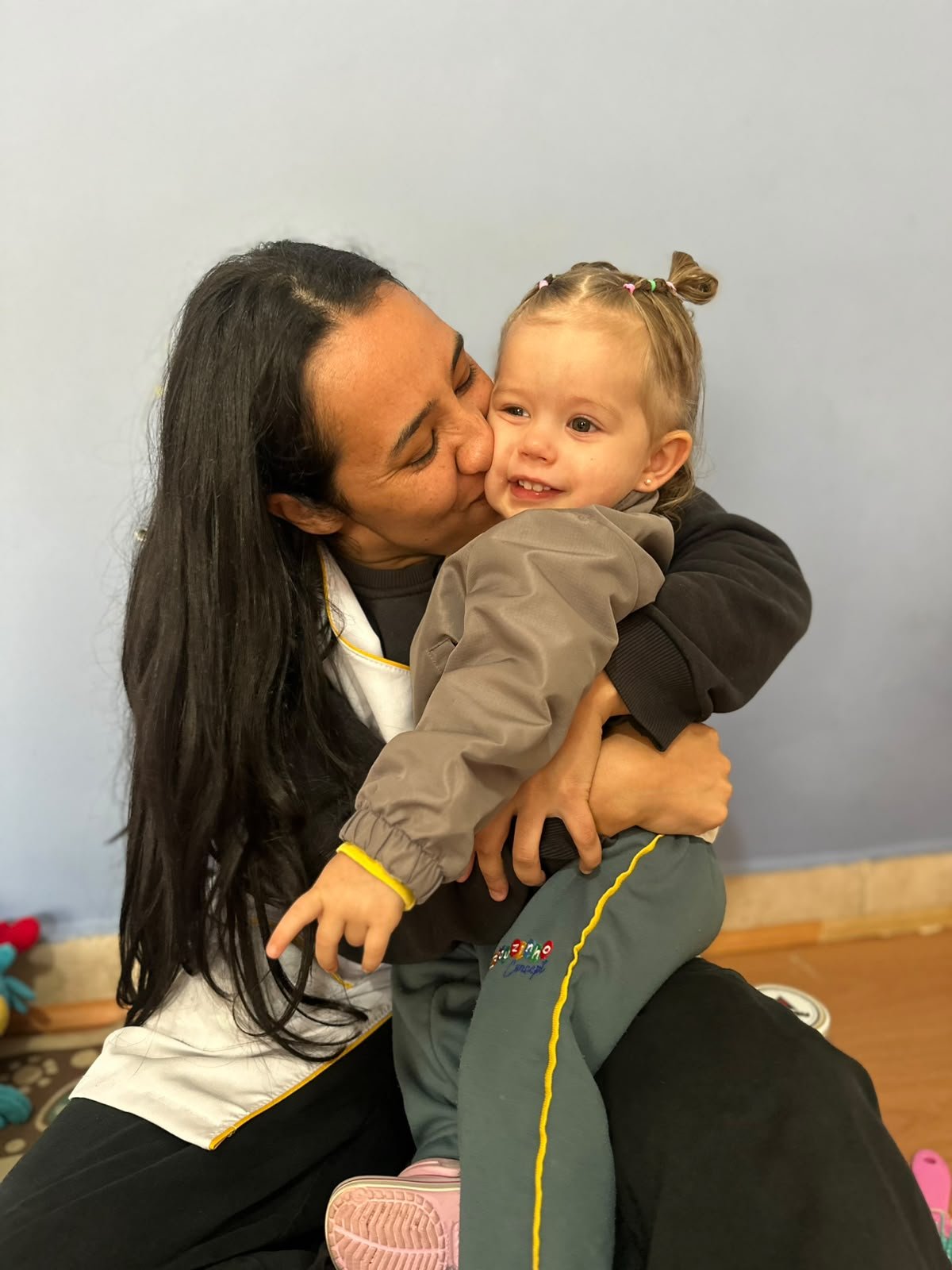 Educadora abraçando e beijando a bochecha de uma menina sorridente