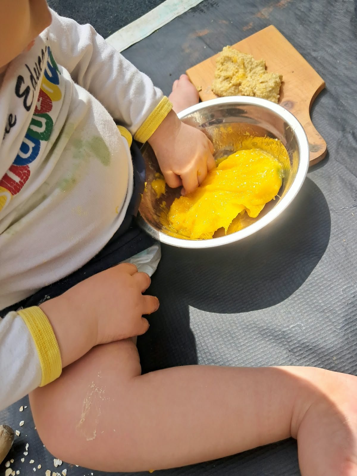 Mãos de bebê explorando uma massa amarela numa tigela