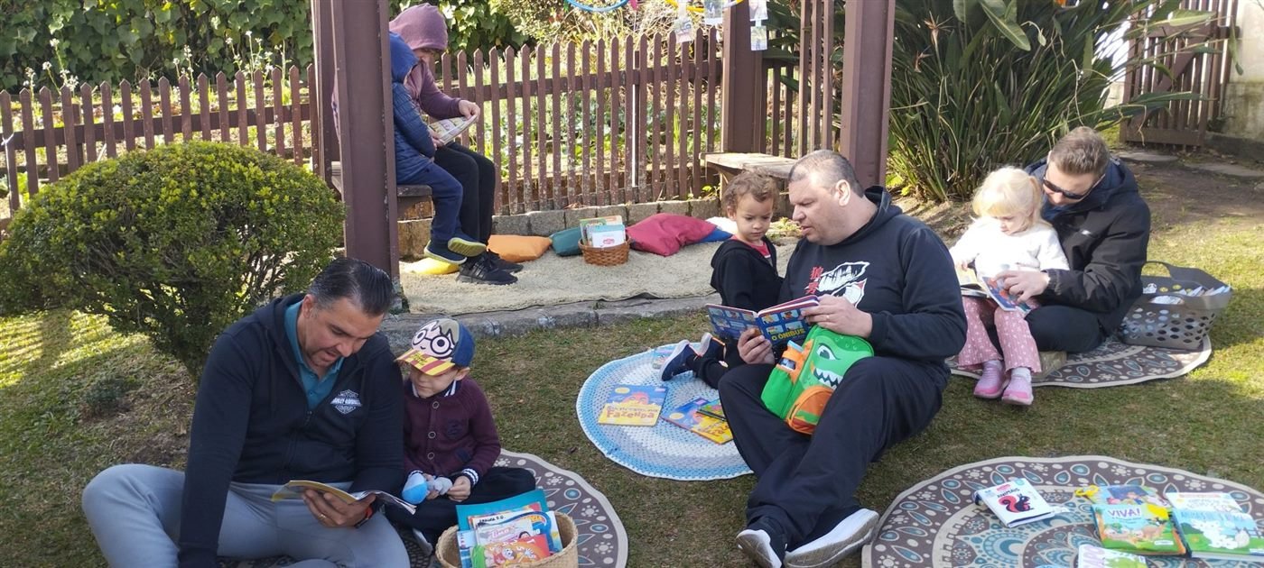 Pais lendo livros com os filhos no gramado da escola