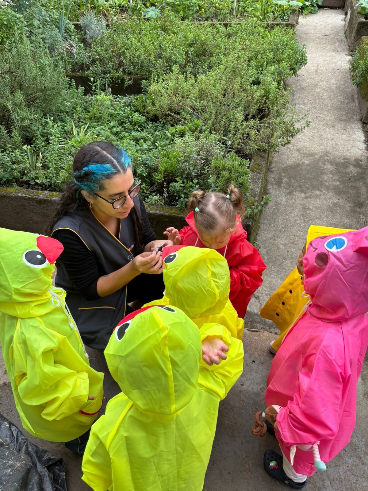 Educadora mostrando um elemento da horta para crianças de capa de chuva